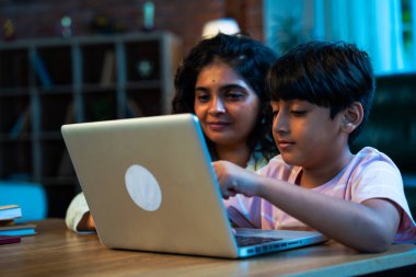 Hintli evlat dizüstü bilgisayar kullanmayı öğrenirken, anne merakla modern evde izliyor, birlikte kaliteli zaman geçiriyorlar, teknolojiyi keşfediyorlar, neşeyi paylaşıyorlar, ebeveyn bağı kuruyorlar, öğrenmeyi büyütüyorlar.