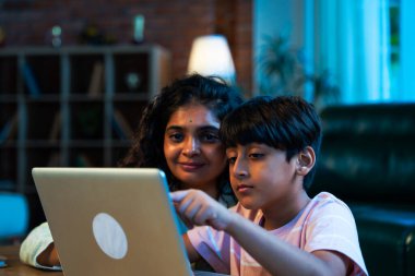 Hintli evlat dizüstü bilgisayar kullanmayı öğrenirken, anne merakla modern evde izliyor, birlikte kaliteli zaman geçiriyorlar, teknolojiyi keşfediyorlar, neşeyi paylaşıyorlar, ebeveyn bağı kuruyorlar, öğrenmeyi büyütüyorlar.