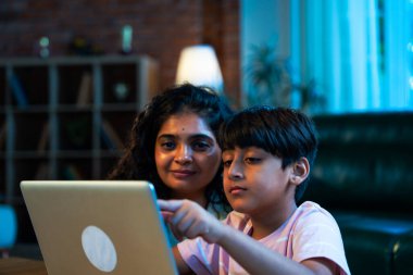 Hintli evlat dizüstü bilgisayar kullanmayı öğrenirken, anne merakla modern evde izliyor, birlikte kaliteli zaman geçiriyorlar, teknolojiyi keşfediyorlar, neşeyi paylaşıyorlar, ebeveyn bağı kuruyorlar, öğrenmeyi büyütüyorlar.