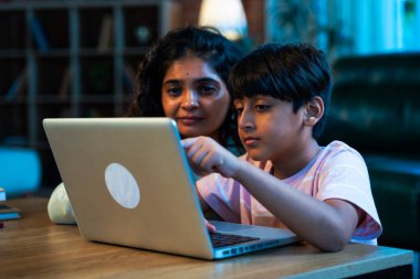 Hintli evlat dizüstü bilgisayar kullanmayı öğrenirken, anne merakla modern evde izliyor, birlikte kaliteli zaman geçiriyorlar, teknolojiyi keşfediyorlar, neşeyi paylaşıyorlar, ebeveyn bağı kuruyorlar, öğrenmeyi büyütüyorlar.