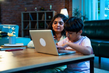 Hintli evlat dizüstü bilgisayar kullanmayı öğrenirken, anne merakla modern evde izliyor, birlikte kaliteli zaman geçiriyorlar, teknolojiyi keşfediyorlar, neşeyi paylaşıyorlar, ebeveyn bağı kuruyorlar, öğrenmeyi büyütüyorlar.