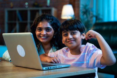 Hintli evlat dizüstü bilgisayar kullanmayı öğrenirken, anne merakla modern evde izliyor, birlikte kaliteli zaman geçiriyorlar, teknolojiyi keşfediyorlar, neşeyi paylaşıyorlar, ebeveyn bağı kuruyorlar, öğrenmeyi büyütüyorlar.