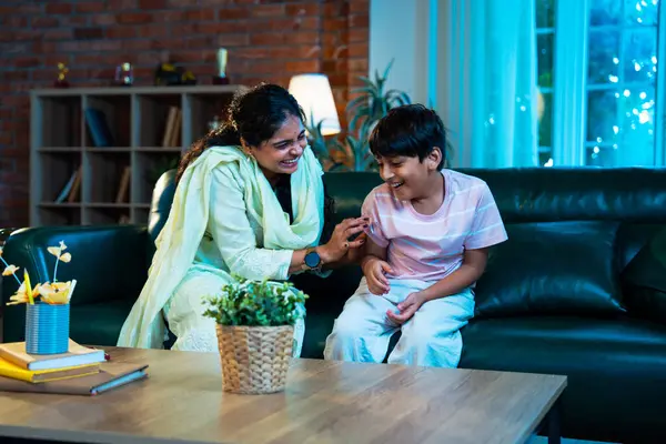 Hintli çocuk ve anne gülerek modern evde kanepede oturuyorlar, birlikte kaliteli zaman geçiriyorlar, şefkat gösteriyorlar, sevgi, neşe, mutluluk, ebeveyn-çocuk ilişkisi yaşam tarzı kapalı