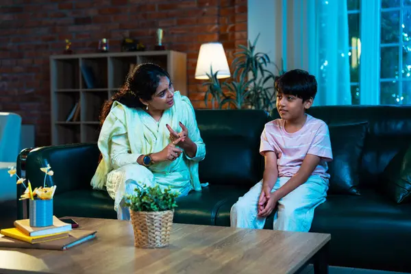 Hintli anne oğlunu azarlıyor, modern evde koltukta otururken, iyi alışkanlıklar öğretiyor, disiplini teşvik ediyor, kaliteli zaman geçirtiyor, çocuğa sevgiyle yol gösteriyor, ebeveyn çocuk ilişkisini kapalı alanda gösteriyor.