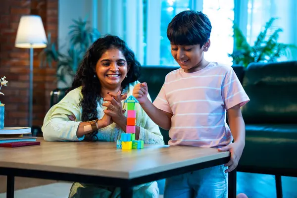 Hintli anne oğul modern evde tahta oyuncak blok kulesi yapıyor, birlikte kaliteli oyun zamanı geçiriyor, yaratıcılık inşa ediyor, eğlenceyi, neşeyi, bağı, ebeveyn çocuk etkileşimini, aile yaşam tarzını evde paylaşıyor.