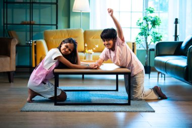 Hintli küçük kardeşler evde bilek güreşi oynuyorlar, Asyalı küçük çocuklar oturma odasında eğlenceli çocukluk aktivitelerinin keyfini çıkarıyorlar, aile bağı, yaşam tarzı, mutluluk.