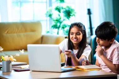 Hintli küçük kardeş evde dizüstü bilgisayarla ders çalışıyor, evde not defteri var, Asyalı küçük çocuklar birlikte öğreniyorlar modern oturma odasında bilgisayar teknolojisi, eğitim ve ev ödevi kullanıyorlar.