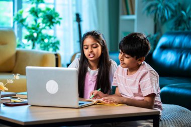 Hintli küçük kardeş evde dizüstü bilgisayarla ders çalışıyor, evde not defteri var, Asyalı küçük çocuklar birlikte öğreniyorlar modern oturma odasında bilgisayar teknolojisi, eğitim ve ev ödevi kullanıyorlar.