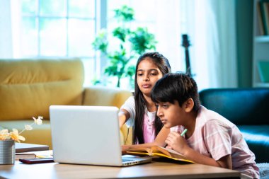 Hintli küçük kardeş evde dizüstü bilgisayarla ders çalışıyor, evde not defteri var, Asyalı küçük çocuklar birlikte öğreniyorlar modern oturma odasında bilgisayar teknolojisi, eğitim ve ev ödevi kullanıyorlar.