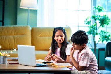 Hintli küçük kardeş evde dizüstü bilgisayarla ders çalışıyor, evde not defteri var, Asyalı küçük çocuklar birlikte öğreniyorlar modern oturma odasında bilgisayar teknolojisi, eğitim ve ev ödevi kullanıyorlar.