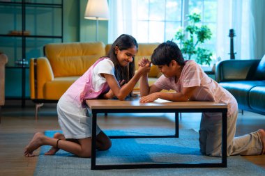 Hintli küçük kardeşler evde bilek güreşi oynuyorlar, Asyalı küçük çocuklar oturma odasında eğlenceli çocukluk aktivitelerinin keyfini çıkarıyorlar, aile bağı, yaşam tarzı, mutluluk.