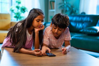 Hintli küçük kardeş akıllı telefon cihazlarıyla oyun oynuyor. Evde boş zaman geçiriyor. Asyalı küçük çocuklar çocukluk aktivitelerinin keyfini çıkarıyorlar.