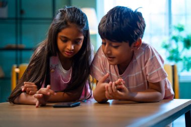 Hintli küçük kardeş akıllı telefon cihazlarıyla oyun oynuyor. Evde boş zaman geçiriyor. Asyalı küçük çocuklar çocukluk aktivitelerinin keyfini çıkarıyorlar.