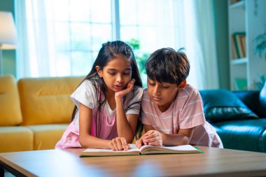 Hintli küçük kardeş evde birlikte kitap okuyor, Asyalı küçük kardeşler öğreniyor, modern oturma odasındaki eğitim aktivitelerine odaklanıyor, aile içinde çocukluk gelişimi.