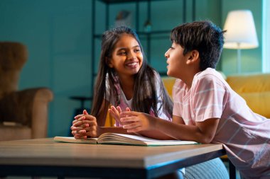 Hintli küçük kardeş evde birlikte kitap okuyor, Asyalı küçük kardeşler öğreniyor, modern oturma odasındaki eğitim aktivitelerine odaklanıyor, aile içinde çocukluk gelişimi.