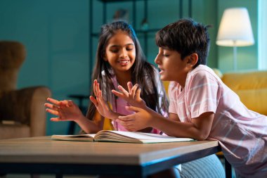 Hintli küçük kardeş evde birlikte kitap okuyor, Asyalı küçük kardeşler öğreniyor, modern oturma odasındaki eğitim aktivitelerine odaklanıyor, aile içinde çocukluk gelişimi.