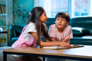 Hintli küçük kardeş evde birlikte kitap okuyor, Asyalı küçük kardeşler öğreniyor, modern oturma odasındaki eğitim aktivitelerine odaklanıyor, aile içinde çocukluk gelişimi.