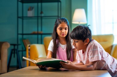 Hintli küçük kardeş evde birlikte kitap okuyor, Asyalı küçük kardeşler öğreniyor, modern oturma odasındaki eğitim aktivitelerine odaklanıyor, aile içinde çocukluk gelişimi.