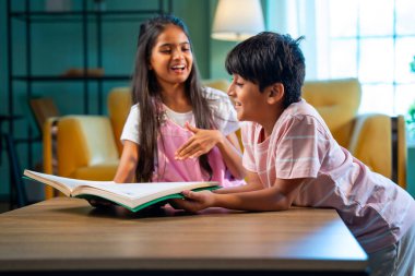Hintli küçük kardeş evde birlikte kitap okuyor, Asyalı küçük kardeşler öğreniyor, modern oturma odasındaki eğitim aktivitelerine odaklanıyor, aile içinde çocukluk gelişimi.