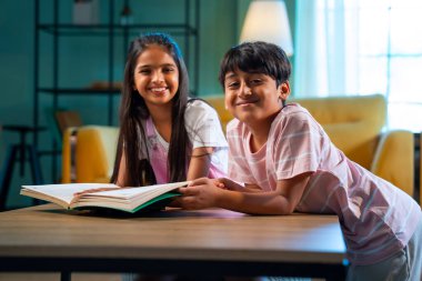 Hintli küçük kardeş evde birlikte kitap okuyor, Asyalı küçük kardeşler öğreniyor, modern oturma odasındaki eğitim aktivitelerine odaklanıyor, aile içinde çocukluk gelişimi.