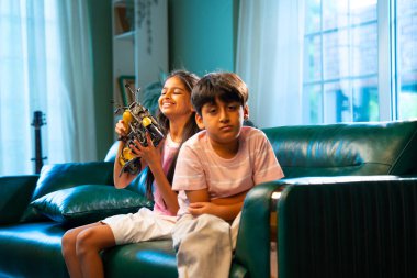 Hintli Asyalı küçük kardeş bisiklet için kavga ederken modern ev içinde kanepede oturan bir çocuk, bir kız ve erkek kardeş tartışırken, kardeş aile bağı, kardeş rekabeti