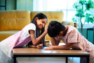 Hintli küçük kardeşler evde bilek güreşi oynuyorlar, Asyalı küçük çocuklar oturma odasında eğlenceli çocukluk aktivitelerinin keyfini çıkarıyorlar, aile bağı, yaşam tarzı, mutluluk.