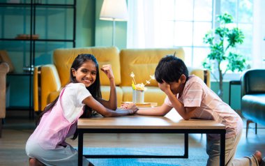 Hintli küçük kardeşler evde bilek güreşi oynuyorlar, Asyalı küçük çocuklar oturma odasında eğlenceli çocukluk aktivitelerinin keyfini çıkarıyorlar, aile bağı, yaşam tarzı, mutluluk.