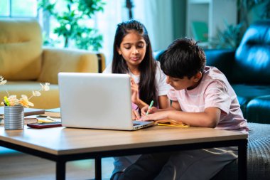 Hintli küçük kardeş evde dizüstü bilgisayarla ders çalışıyor, evde not defteri var, Asyalı küçük çocuklar birlikte öğreniyorlar modern oturma odasında bilgisayar teknolojisi, eğitim ve ev ödevi kullanıyorlar.