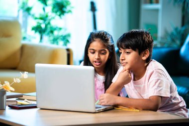 Hintli küçük kardeş evde dizüstü bilgisayarla ders çalışıyor, evde not defteri var, Asyalı küçük çocuklar birlikte öğreniyorlar modern oturma odasında bilgisayar teknolojisi, eğitim ve ev ödevi kullanıyorlar.