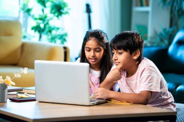 Hintli küçük kardeş evde dizüstü bilgisayarla ders çalışıyor, evde not defteri var, Asyalı küçük çocuklar birlikte öğreniyorlar modern oturma odasında bilgisayar teknolojisi, eğitim ve ev ödevi kullanıyorlar.