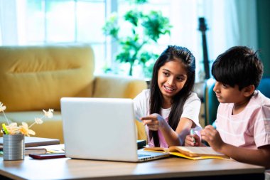 Hintli küçük kardeş evde dizüstü bilgisayarla ders çalışıyor, evde not defteri var, Asyalı küçük çocuklar birlikte öğreniyorlar modern oturma odasında bilgisayar teknolojisi, eğitim ve ev ödevi kullanıyorlar.
