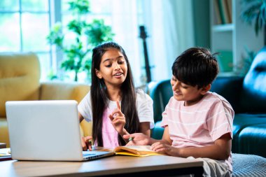 Hintli küçük kardeş evde dizüstü bilgisayarla ders çalışıyor, evde not defteri var, Asyalı küçük çocuklar birlikte öğreniyorlar modern oturma odasında bilgisayar teknolojisi, eğitim ve ev ödevi kullanıyorlar.