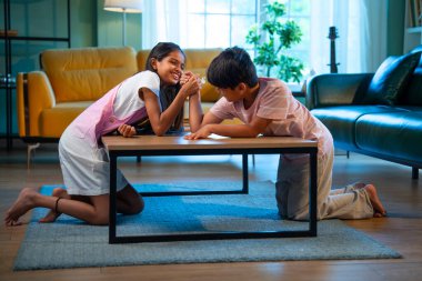 Hintli küçük kardeşler evde bilek güreşi oynuyorlar, Asyalı küçük çocuklar oturma odasında eğlenceli çocukluk aktivitelerinin keyfini çıkarıyorlar, aile bağı, yaşam tarzı, mutluluk.