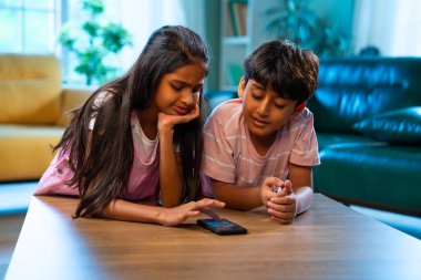 Hintli küçük kardeş akıllı telefon cihazlarıyla oyun oynuyor. Evde boş zaman geçiriyor. Asyalı küçük çocuklar çocukluk aktivitelerinin keyfini çıkarıyorlar.