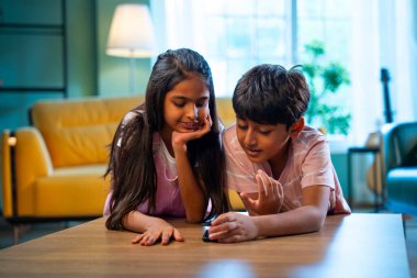 Hintli küçük kardeş akıllı telefon cihazlarıyla oyun oynuyor. Evde boş zaman geçiriyor. Asyalı küçük çocuklar çocukluk aktivitelerinin keyfini çıkarıyorlar.