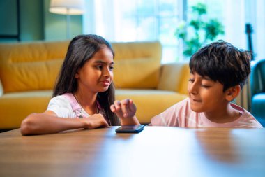 Hintli küçük kardeş akıllı telefon cihazlarıyla oyun oynuyor. Evde boş zaman geçiriyor. Asyalı küçük çocuklar çocukluk aktivitelerinin keyfini çıkarıyorlar.