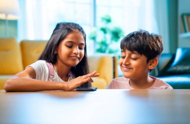 Hintli küçük kardeş akıllı telefon cihazlarıyla oyun oynuyor. Evde boş zaman geçiriyor. Asyalı küçük çocuklar çocukluk aktivitelerinin keyfini çıkarıyorlar.