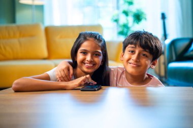 Hintli küçük kardeş akıllı telefon cihazlarıyla oyun oynuyor. Evde boş zaman geçiriyor. Asyalı küçük çocuklar çocukluk aktivitelerinin keyfini çıkarıyorlar.