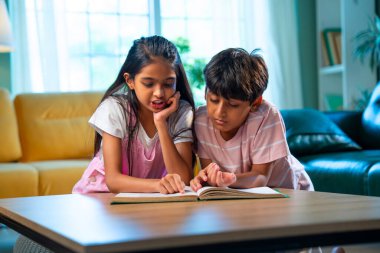 Hintli küçük kardeş evde birlikte kitap okuyor, Asyalı küçük kardeşler öğreniyor, modern oturma odasındaki eğitim aktivitelerine odaklanıyor, aile içinde çocukluk gelişimi.