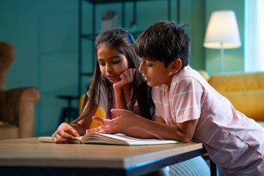 Hintli küçük kardeş evde birlikte kitap okuyor, Asyalı küçük kardeşler öğreniyor, modern oturma odasındaki eğitim aktivitelerine odaklanıyor, aile içinde çocukluk gelişimi.