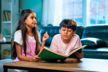 Hintli küçük kardeş evde birlikte kitap okuyor, Asyalı küçük kardeşler öğreniyor, modern oturma odasındaki eğitim aktivitelerine odaklanıyor, aile içinde çocukluk gelişimi.
