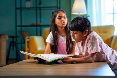 Hintli küçük kardeş evde birlikte kitap okuyor, Asyalı küçük kardeşler öğreniyor, modern oturma odasındaki eğitim aktivitelerine odaklanıyor, aile içinde çocukluk gelişimi.