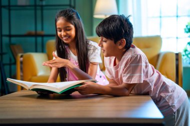 Hintli küçük kardeş evde birlikte kitap okuyor, Asyalı küçük kardeşler öğreniyor, modern oturma odasındaki eğitim aktivitelerine odaklanıyor, aile içinde çocukluk gelişimi.