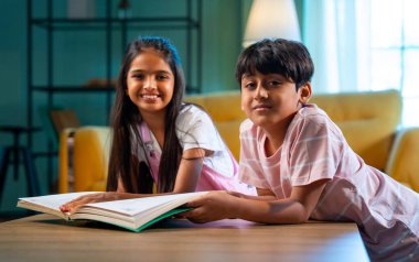 Hintli küçük kardeş evde birlikte kitap okuyor, Asyalı küçük kardeşler öğreniyor, modern oturma odasındaki eğitim aktivitelerine odaklanıyor, aile içinde çocukluk gelişimi.