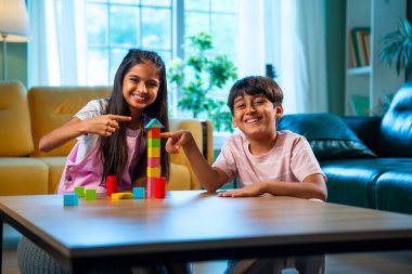 Hintli küçük kardeş evde birlikte ahşap oyuncak kulesi inşa ediyor, Asyalı küçük çocuklar çocukluk aktivitelerinin keyfini çıkarıyorlar, aile bağlarıyla modern evde kaliteli zaman geçiriyorlar.