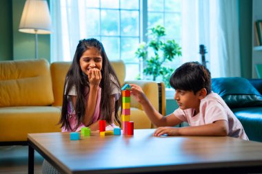 Hintli küçük kardeş evde birlikte ahşap oyuncak kulesi inşa ediyor, Asyalı küçük çocuklar çocukluk aktivitelerinin keyfini çıkarıyorlar, aile bağlarıyla modern evde kaliteli zaman geçiriyorlar.