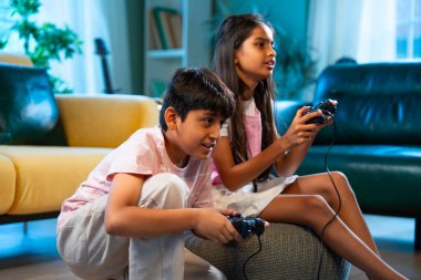 Hintli Asyalı küçük çocuklar evde joystick kontrolörüyle video oyunu oynuyorlar, evde kardeşçe eğlenceli vakit geçiriyorlar, çocukluk eğlenceleri, modern yaşam tarzı dijital eğlence.