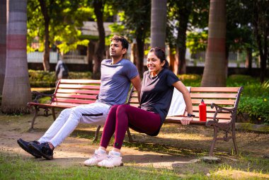 Hindistan 'ın güzel çifti, yeşil doğa ortamında güneşli bir günde parkta birlikte spor yaparken bankta triseps dalışı yapıyor. Sağlık, spor ve güçlü ilişki hedeflerini gösteriyor.