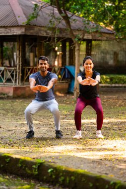 Hintli güzel genç çift güneşli bir günde parkın dışında birlikte çömeliyorlar. Günlük fitness rutinlerinin bir parçası olarak, güç, sağlık, motivasyon ve aktif sağlıklı yaşam tarzı hedeflerine odaklanıyorlar.