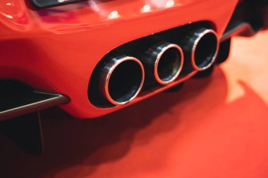 detail rear view of red sport car triple exhaust pipes
